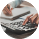Image contains a person calculating numbers on a calculator and writing on a pad of paper with a pen.