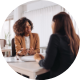 Image shows a woman talking with another woman behind a desk.